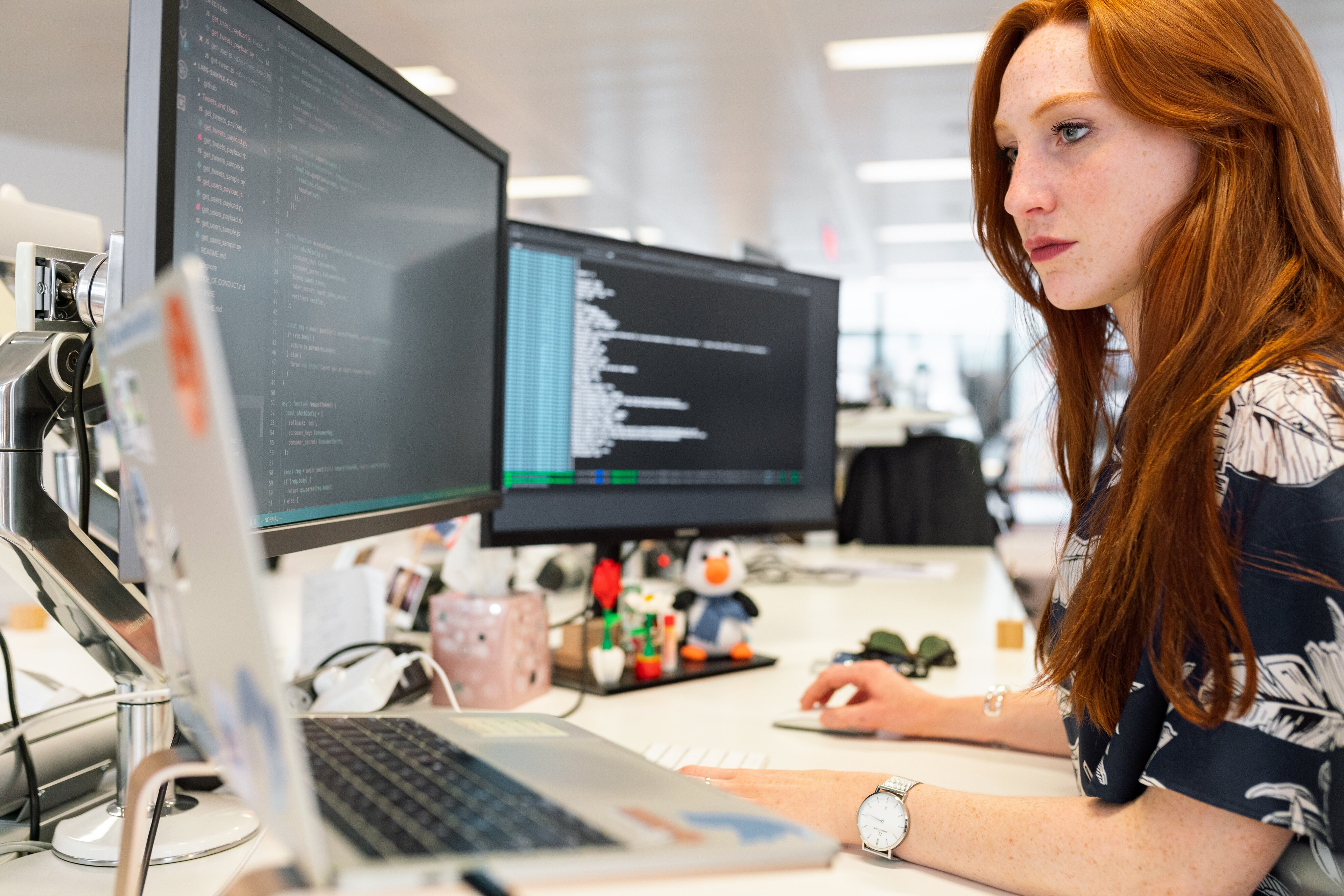 A woman working at a desk with a laptop and two computer screens