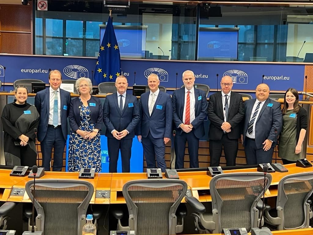 The delegation standing in a chamber within the European Parliament.