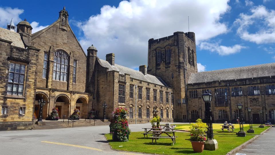 Old stone building built around a lawn with picnic benches and old fashioned lamp posts