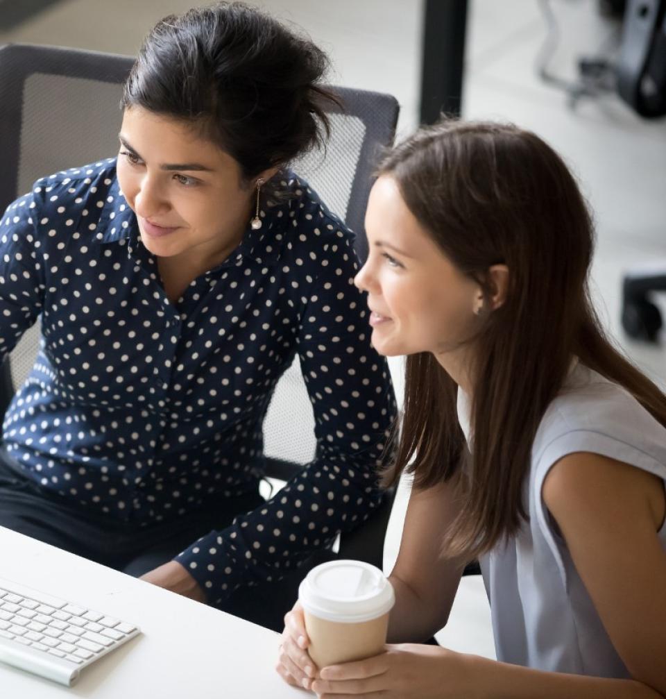 Two women, one holding a coffee, working on a computer