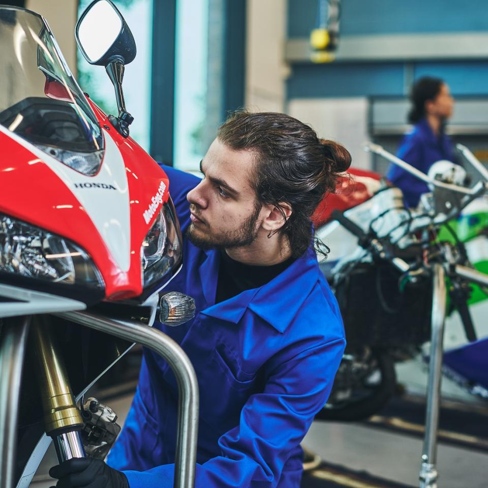 A mechanic in blue overalls is working on a motorbike