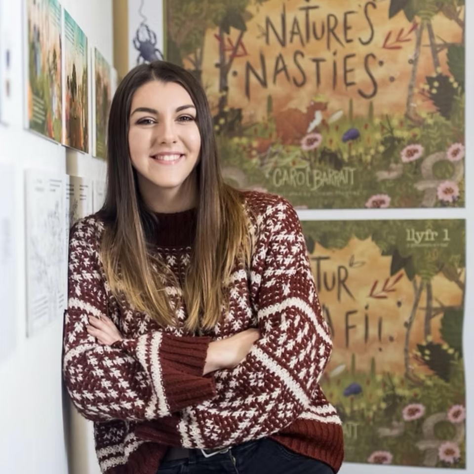 Ocean Hughes standing in front of a wall with illustrated posters