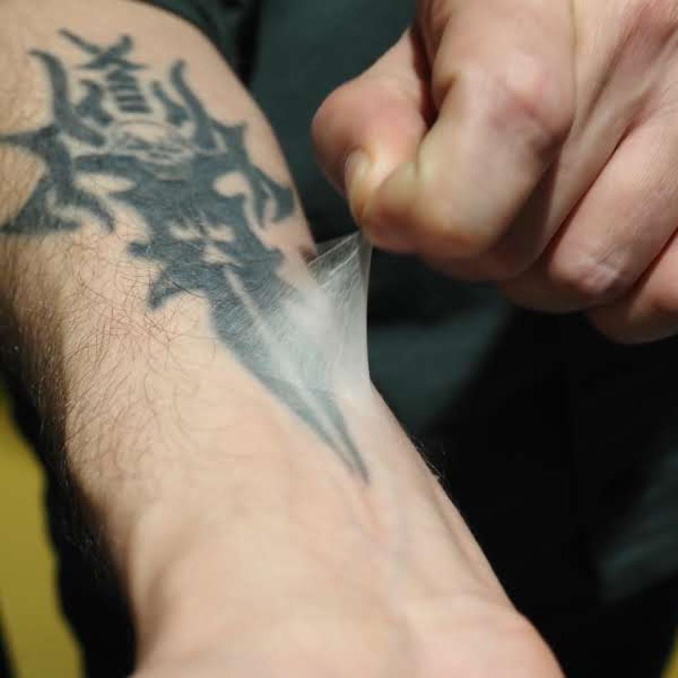 A close up shot of someone's hand pulling a clear film off their tattooed arm