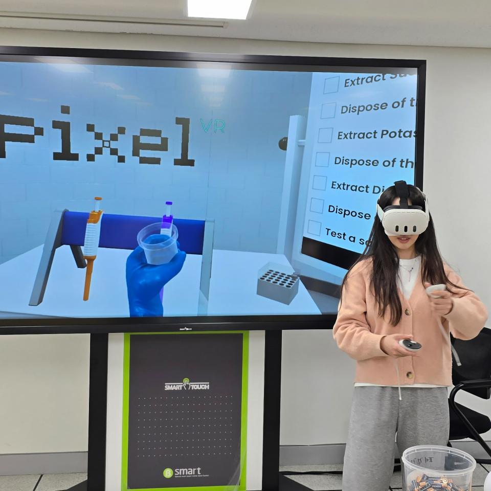 A woman wearing a VR headset standing in front of a large screen which shows a laboratory setting