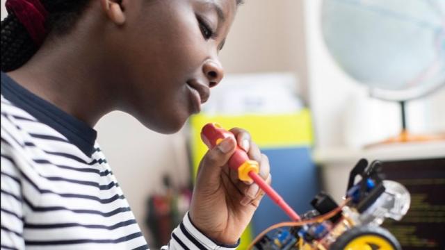 Young woman in stripy top using a screwdriver to work on an electric model car