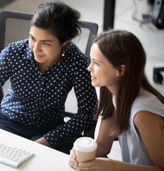 Two women, one holding a coffee, working on a computer
