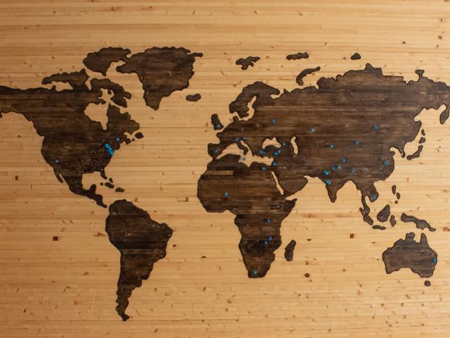 A map of the world on a wooden background with blue pins stuck in lots of countries