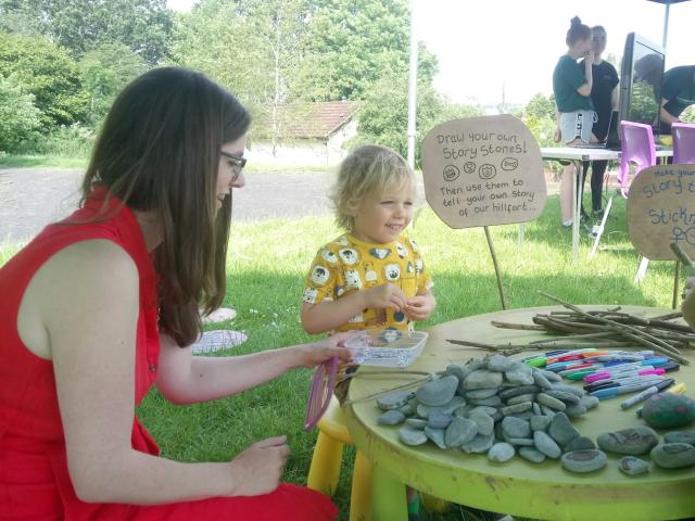 A woman in a red dress with a young child in a yellow top, sitting outside sorting through stones on a table