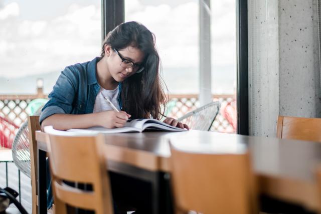 A young woman studying at a table in front of windows