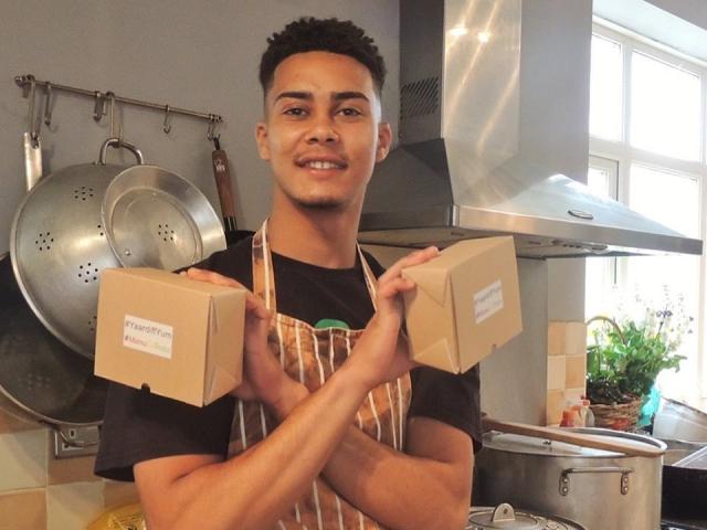 Man in kitchen wearing an apron and holding two food boxes
