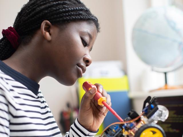Young woman in stripy top using a screwdriver to work on an electric model car