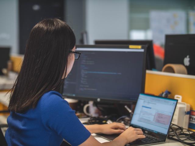 Young woman in blue top sitting at a desk working on a computer