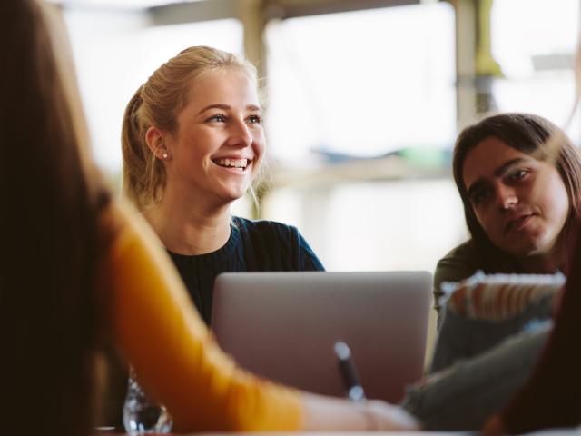 Woman with blonde hair smiling, sitting in front of a laptop