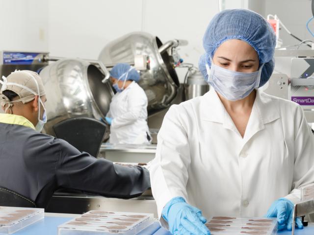 Woman in white coat, hair covering and face mask working in a food factory