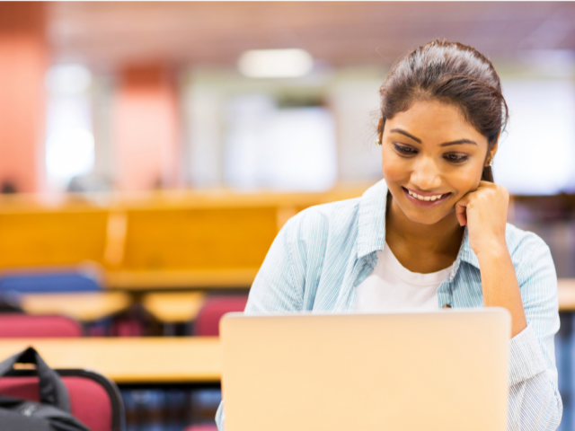 Young woman smiling and working on a laptop in a library