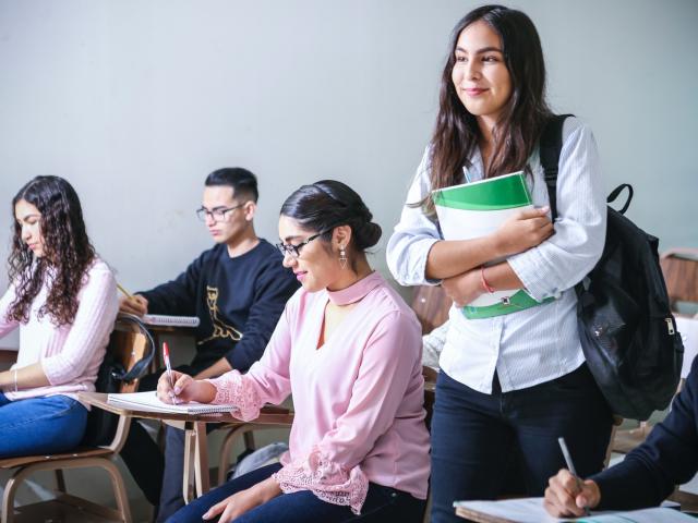 Young woman holding a book walking through a class of students