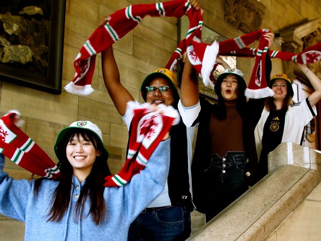 International students cheering and waving Wales scarves. 