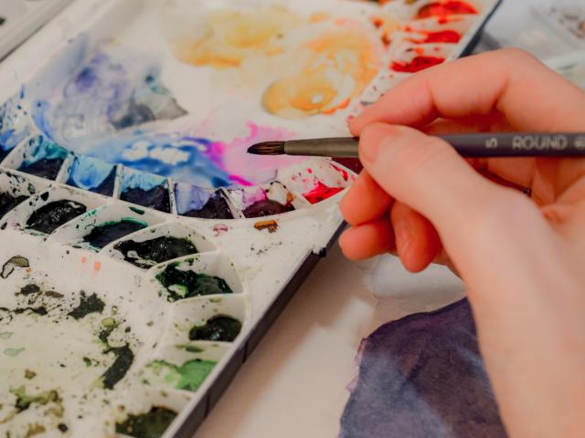 Close up shot of someone holding a paintbrush over a palette of paints