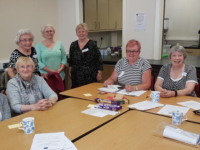 A group of smiling women sitting and standing around a meeting table