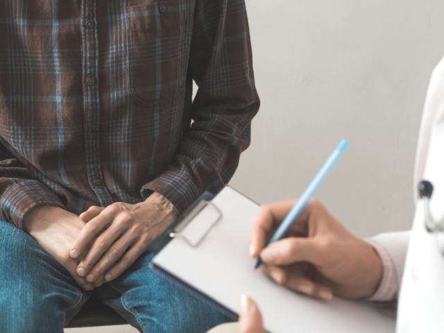 A man sitting on a bed with a doctor writing on a clipboard