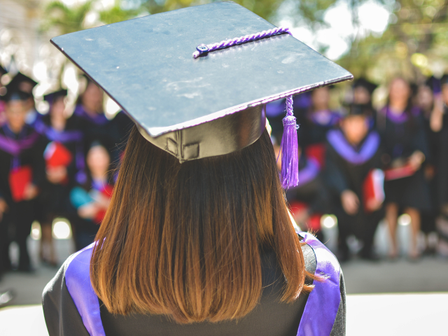 A graduate in cap and gown with back to camera, facing a crowd of other graduates