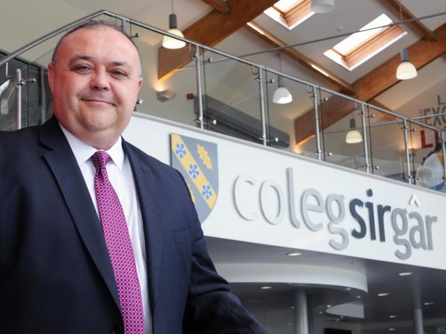 Dr Andrew Cornish standing in front of a Coleg Sir Gar sign