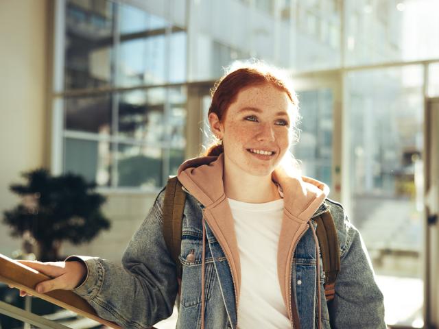 A smiling young woman standing in front of large windows