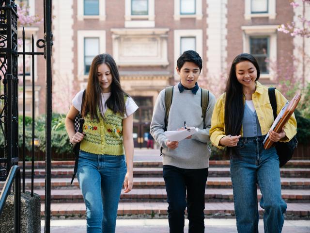 three students (one man, two women) walking together outside a building