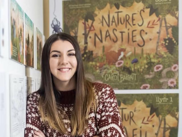 Ocean Hughes standing in front of a wall with illustrated posters