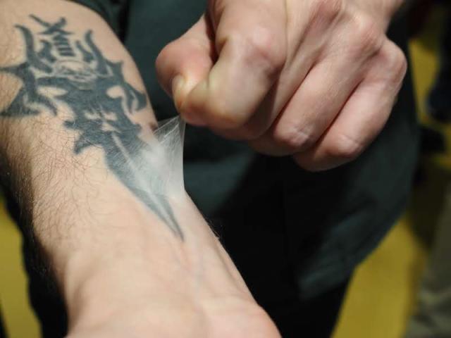 A close up shot of someone's hand pulling a clear film off their tattooed arm