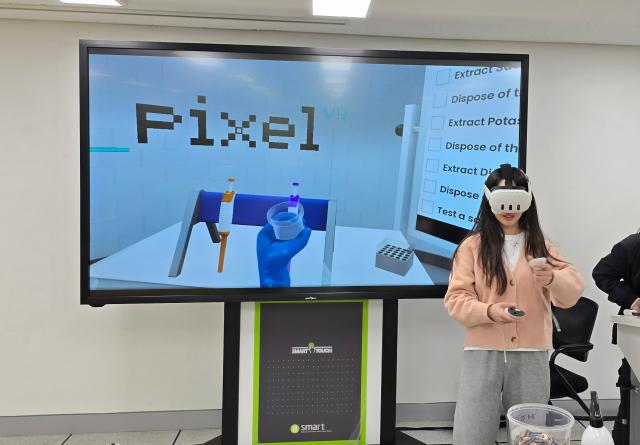 A woman wearing a VR headset standing in front of a large screen which shows a laboratory setting